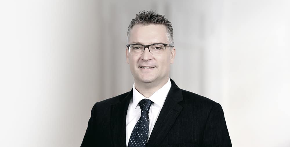 Wolfgang Amann professional corporate portrait in business suit and glasses.