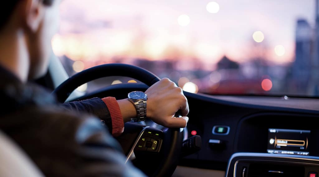 Driver wearing wristwatch grips steering wheel in modern car at city night.
