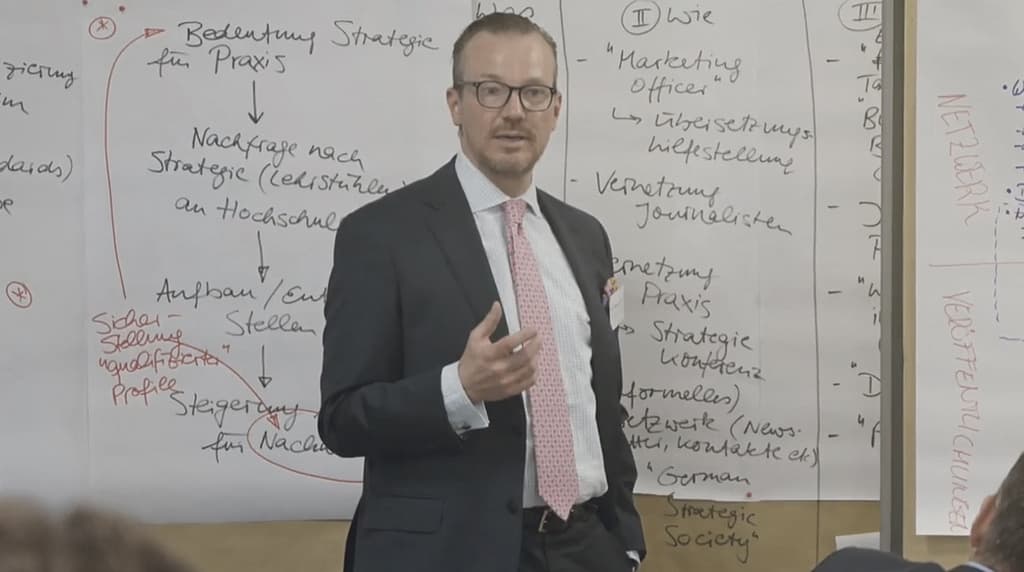Dr. Thomas K. Hamann is explaining the Scientific Commission of Strategic Management's plans to the audience on a whiteboard.