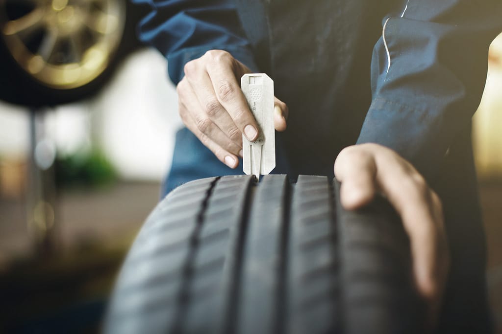 Mechanic checking tire tread depth with gauge during vehicle maintenance.
