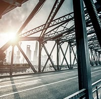 Steel truss bridge toward a city skyline representing cross-industry transfers.