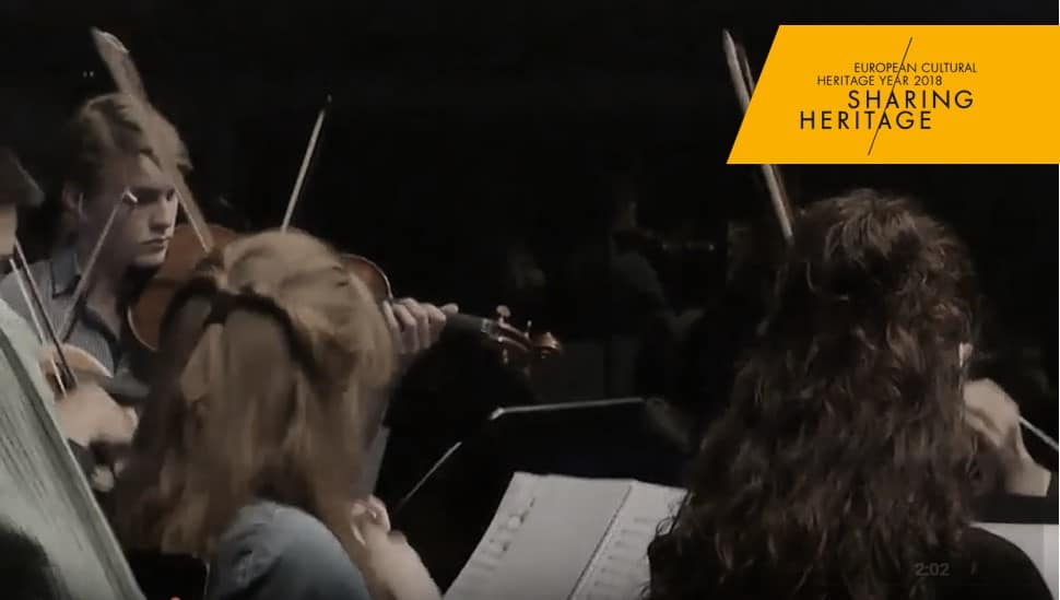 String ensemble performs contemporary music with violins, bows, sheet music, and Sharing Heritage banner.